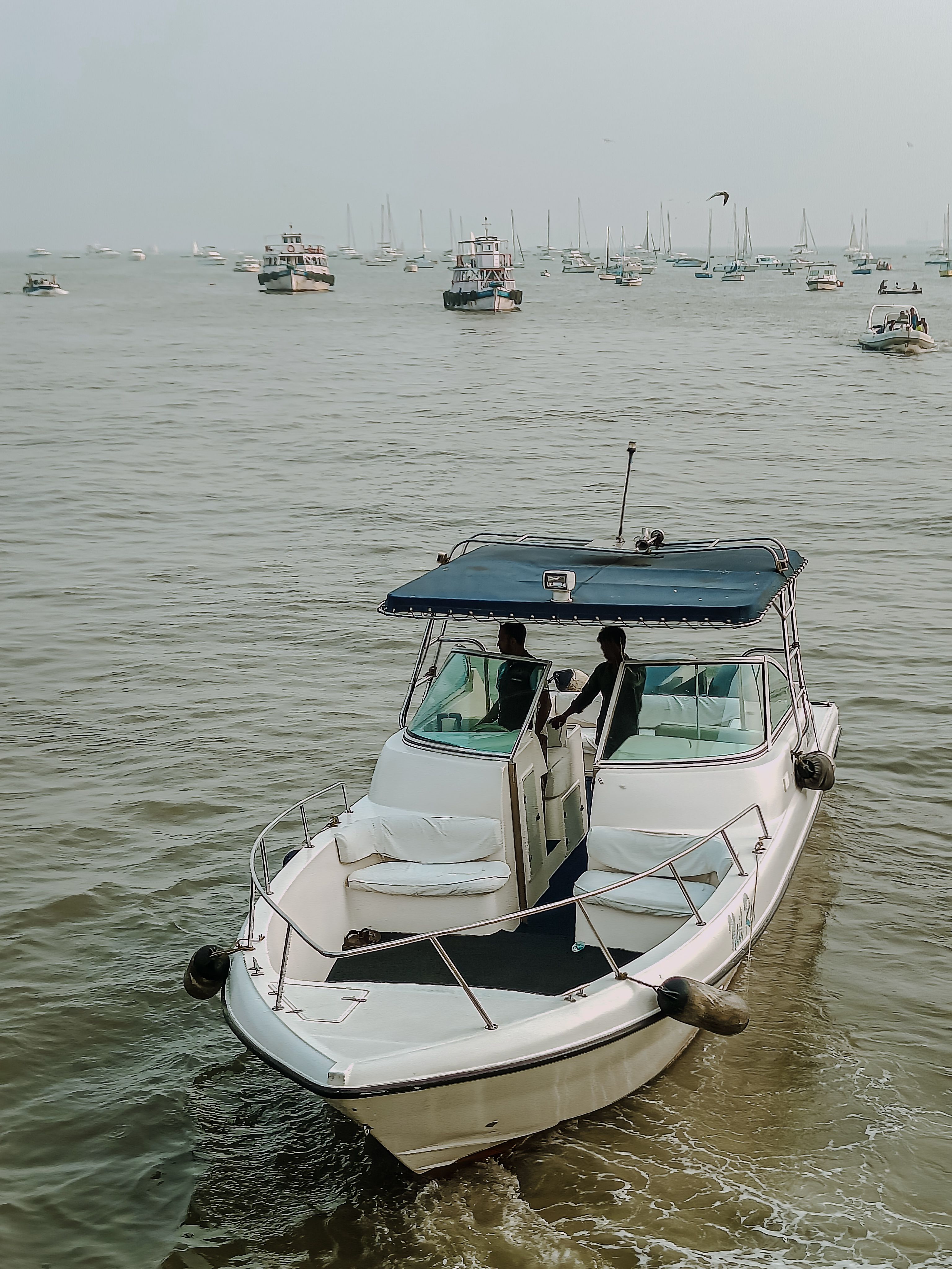 Two individuals on a motorboat in Mumbai's bustling waters with numerous boats in the background.