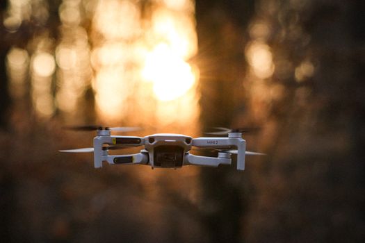 A modern drone flying against a sunlit forest backdrop, capturing nature's beauty.