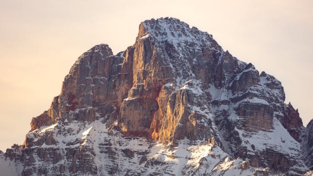 Majestic Dolomite mountain during sunset, highlighting snowy cliffs and warm tones.