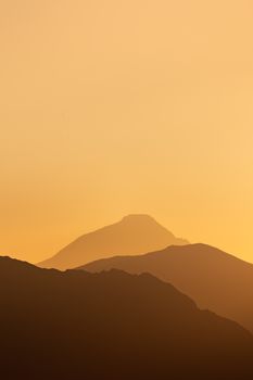 A tranquil sunrise with layers of misty mountains silhouetted against a warm orange sky.