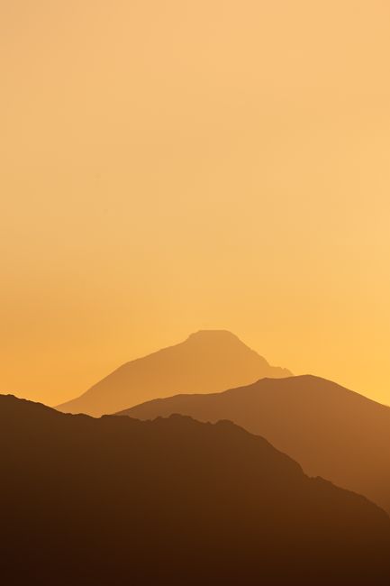 A tranquil sunrise with layers of misty mountains silhouetted against a warm orange sky.