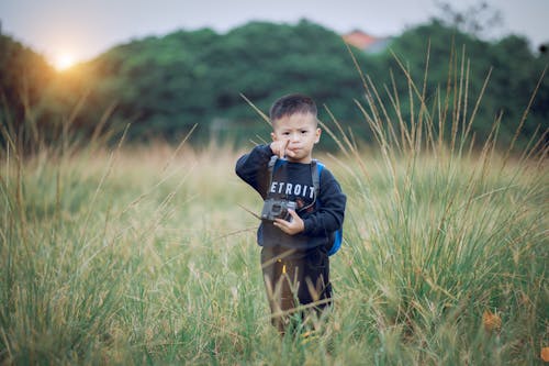 Boy Standing on Green Field Holding Black Camera