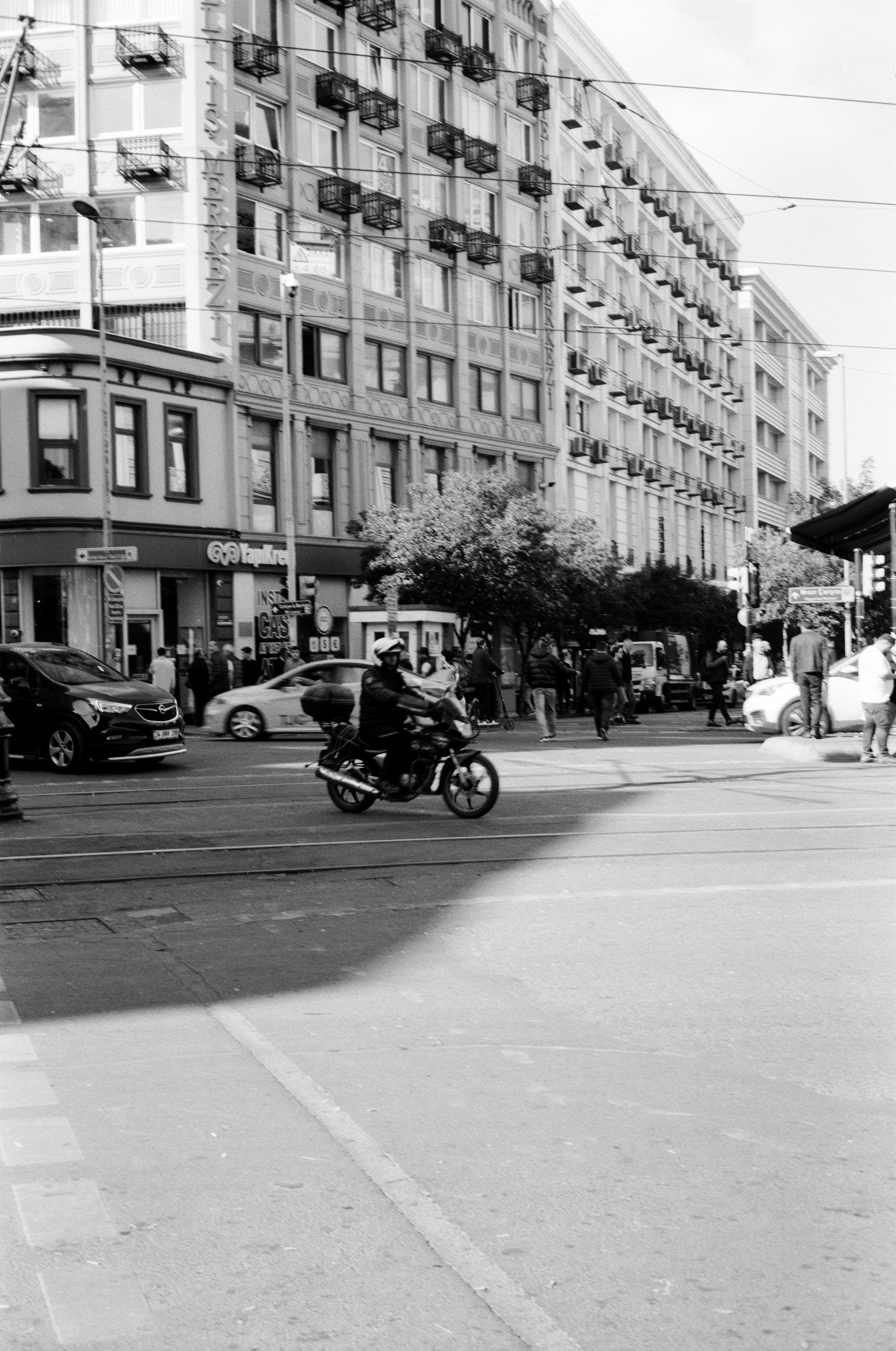 Urban street scene in İstanbul with motorbike, cars, and pedestrians crossing a busy intersection.