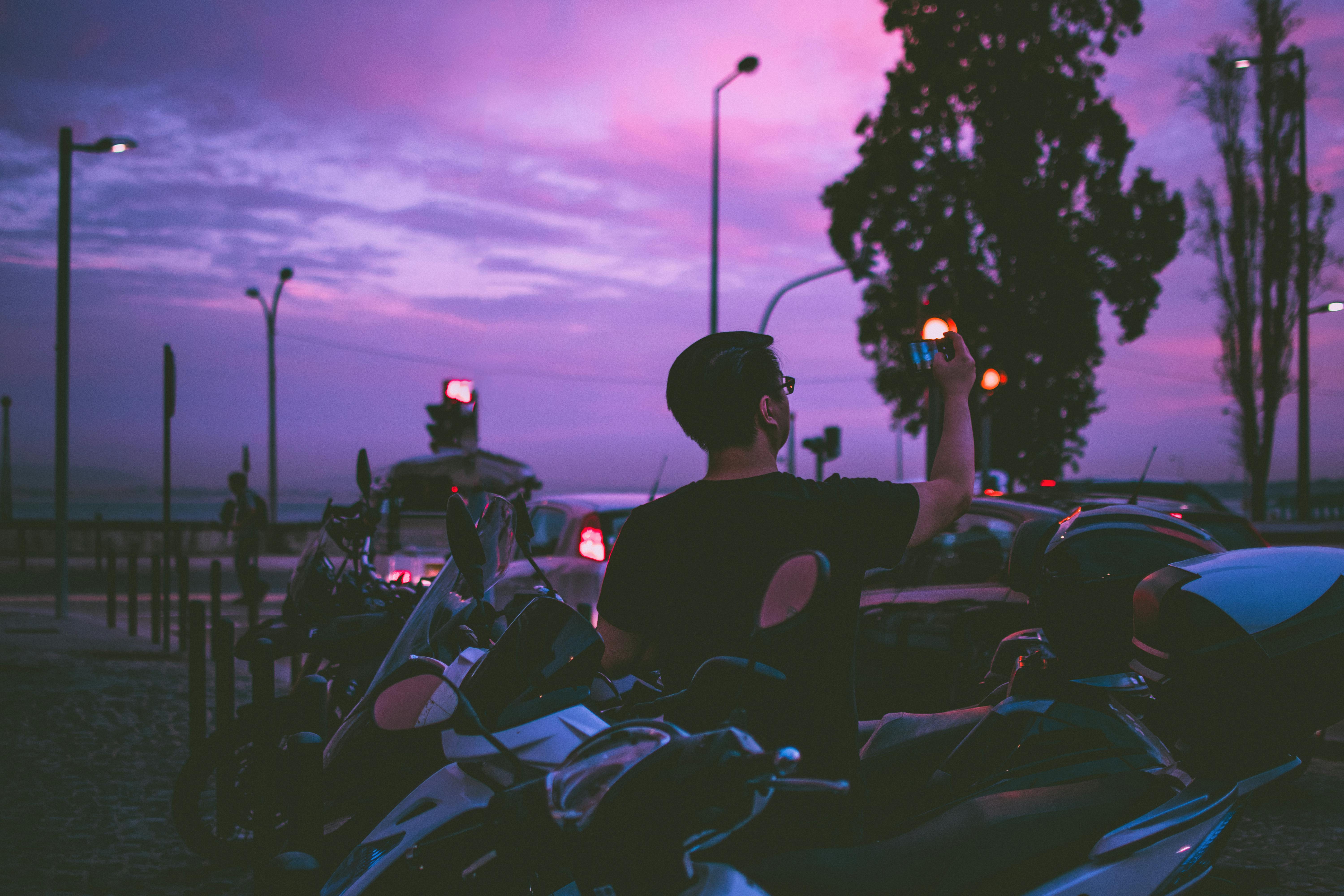 A man capturing the vibrant sunset skyline amidst motorcycles in an urban setting.
