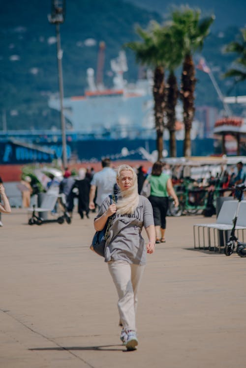 Young Woman Walking on a Pavement with the Harbor behind Her 