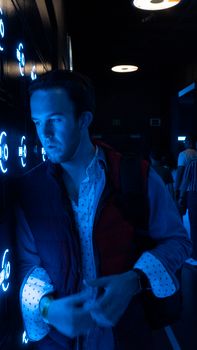 A man standing in a dimly lit room with blue neon light reflections on the walls.