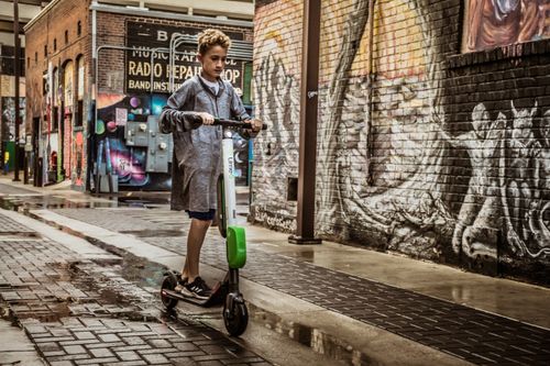 Free Child riding an electric scooter through a graffiti-covered urban alleyway. Stock Photo