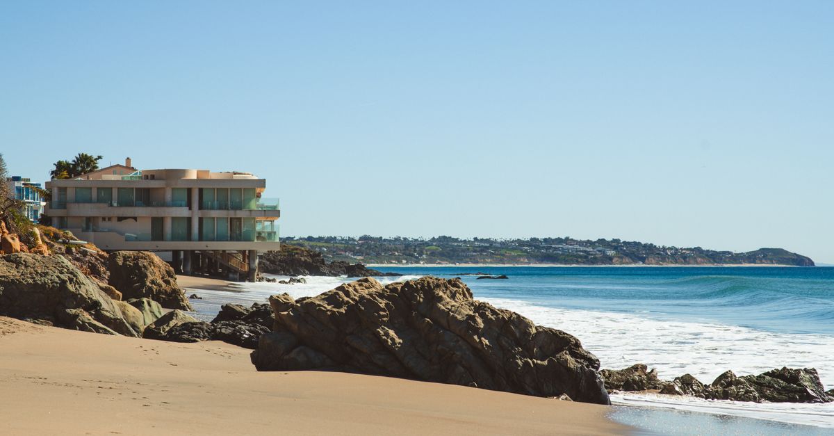 Stylish beach house overlooking the ocean, surrounded by rocks and sandy shores.