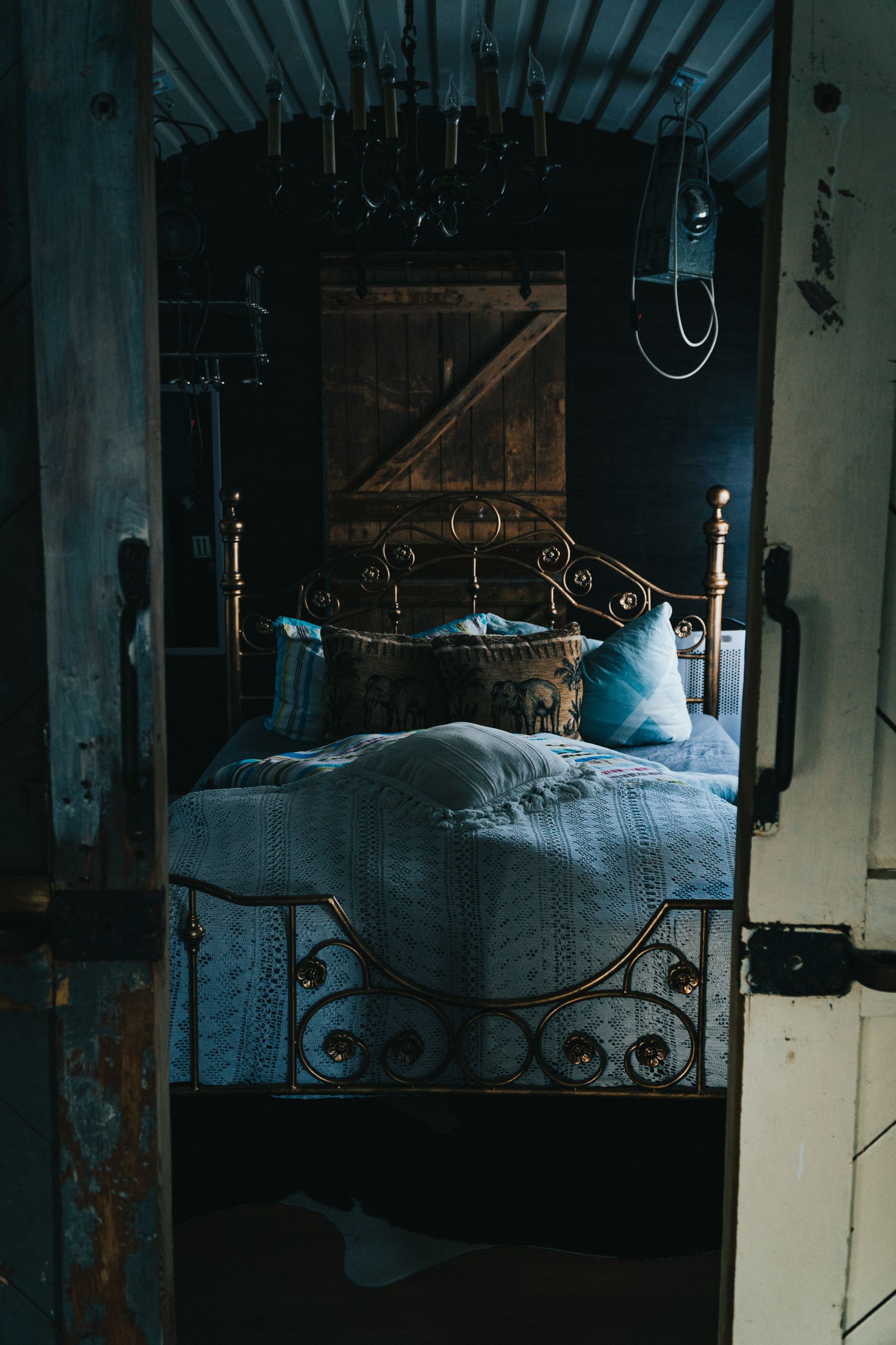 Gold-colored scrollwork metal bed with layered blue textiles in a dark rustic room