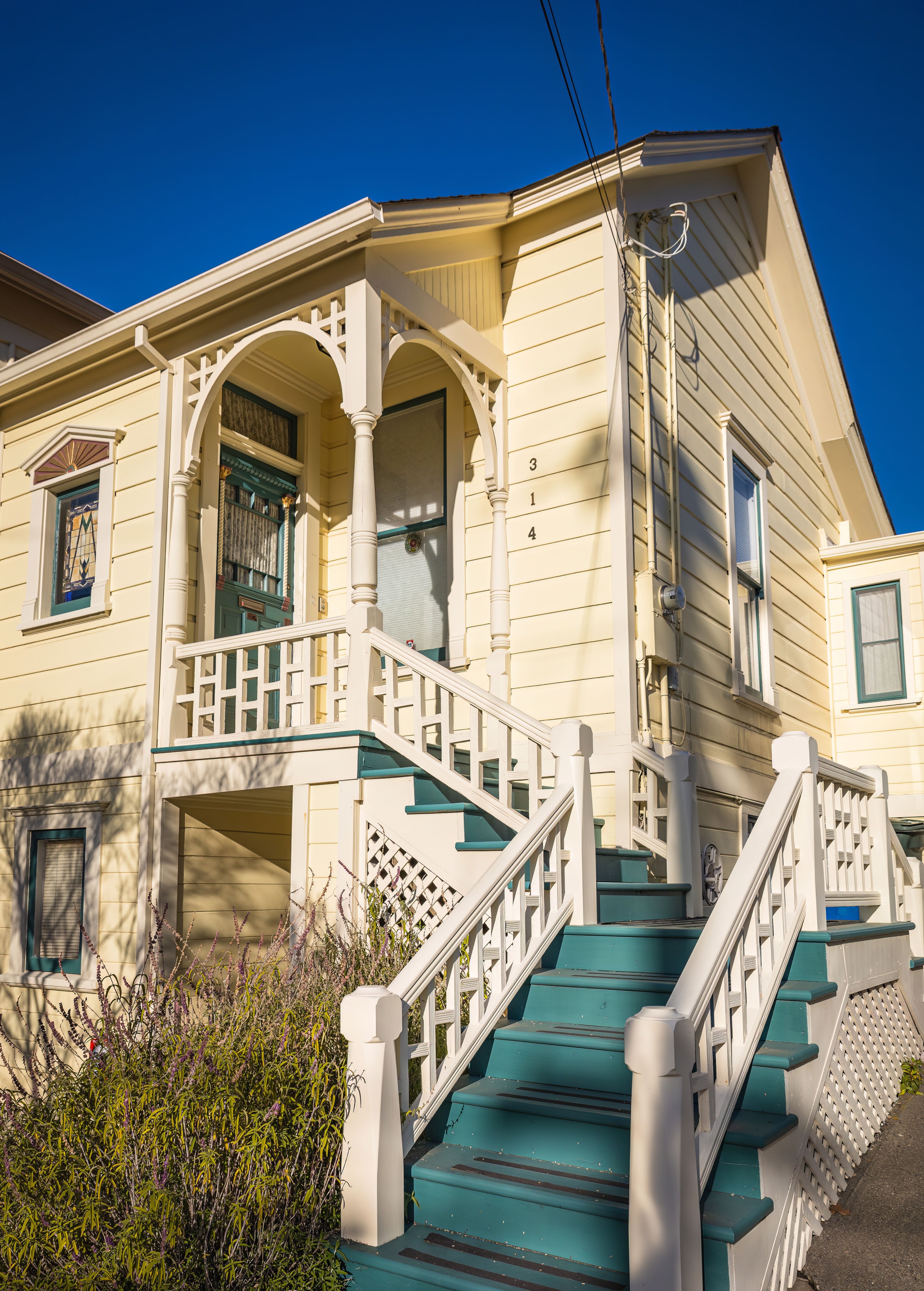 Picturesque yellow cottage with blue steps and ornate balustrades under a clear blue sky.