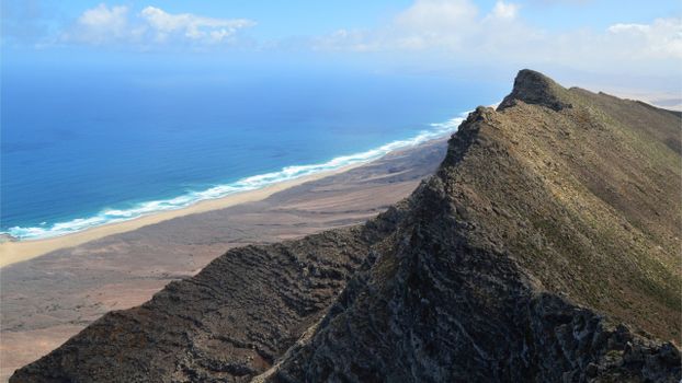 A stunning view of a rocky cliff overlooking the turquoise ocean and beach under a clear sky.