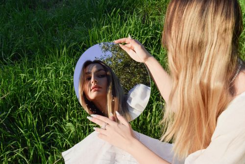 Free Woman with long hair holding a round mirror reflects face in lush green meadow. Stock Photo