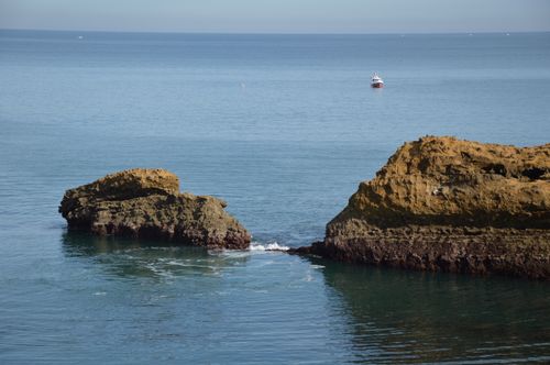 Free Peaceful coastal seascape featuring rocky formations and a distant boat on a clear day. Stock Photo