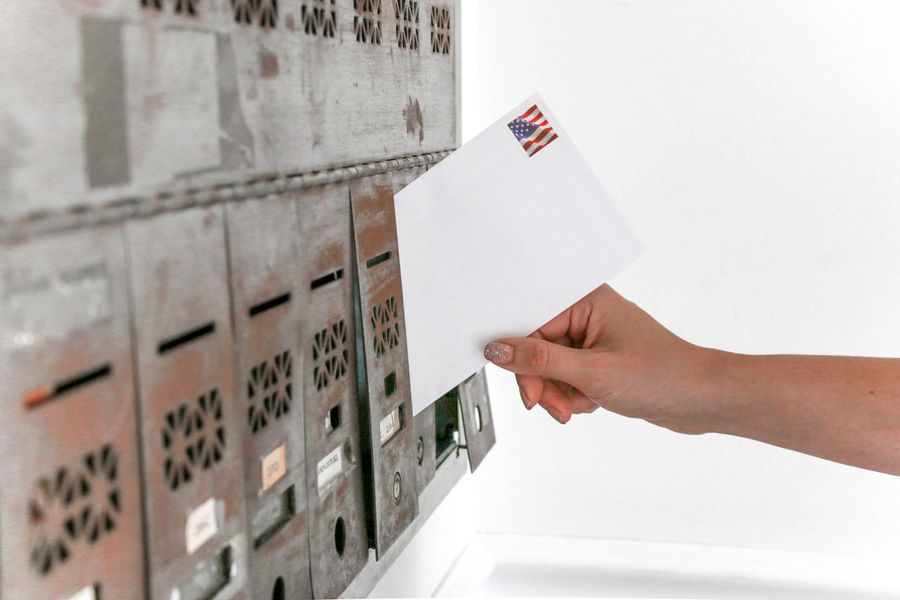 A hand inserting a stamped envelope into a mailbox