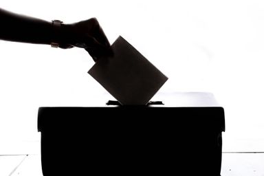 A hand posting a folded paper ballot into a sealed box