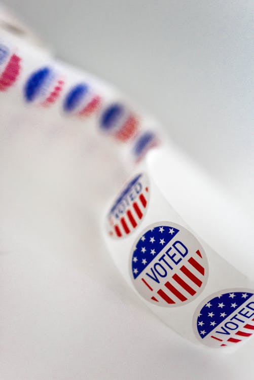 Closeup of tape with round stickers with I voted inscription and flag of United States of America against white background