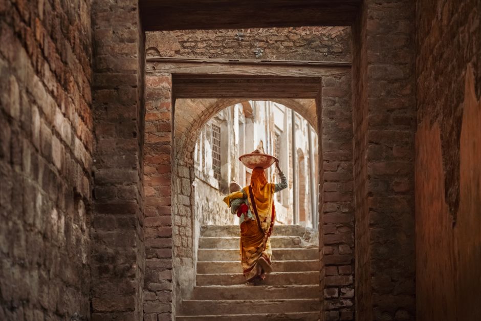 A woman in traditional attire carrying goods in a historic town's stone passageway.