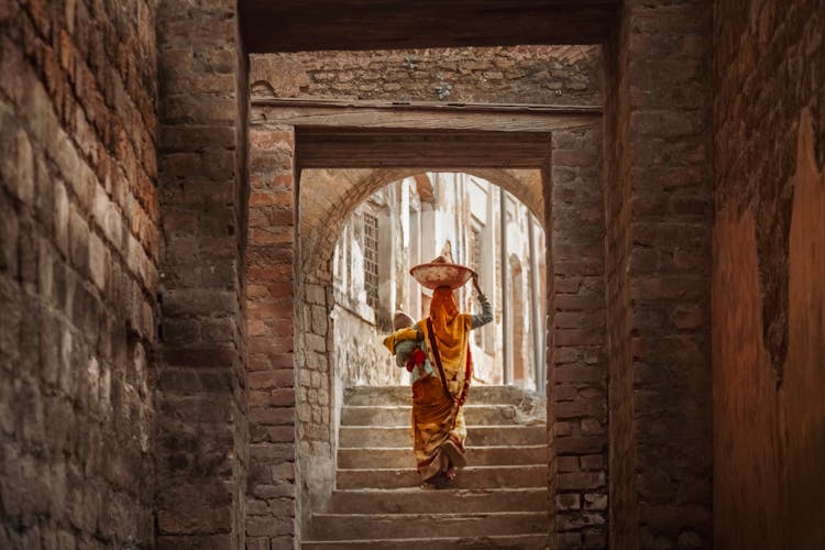 Woman In Traditional Dress Carrying Load On Stone Old Street