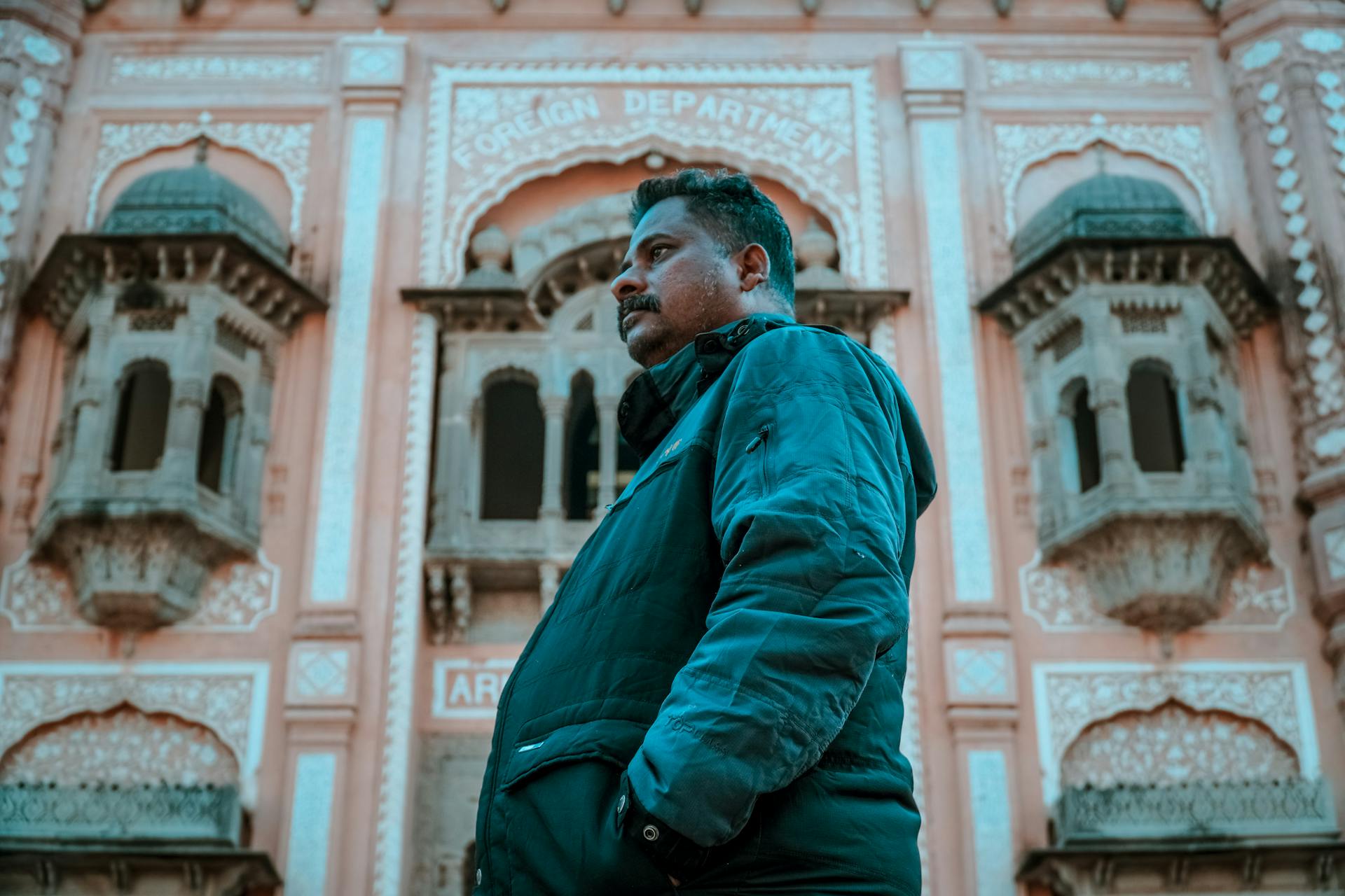 A man in a jacket stands in front of a historical foreign department building facade.