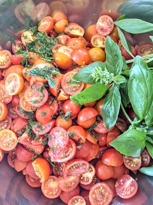 Free Sliced Red Cherry Tomatoes and Fresh Basil in a Metal Salad Bowl Stock Photo