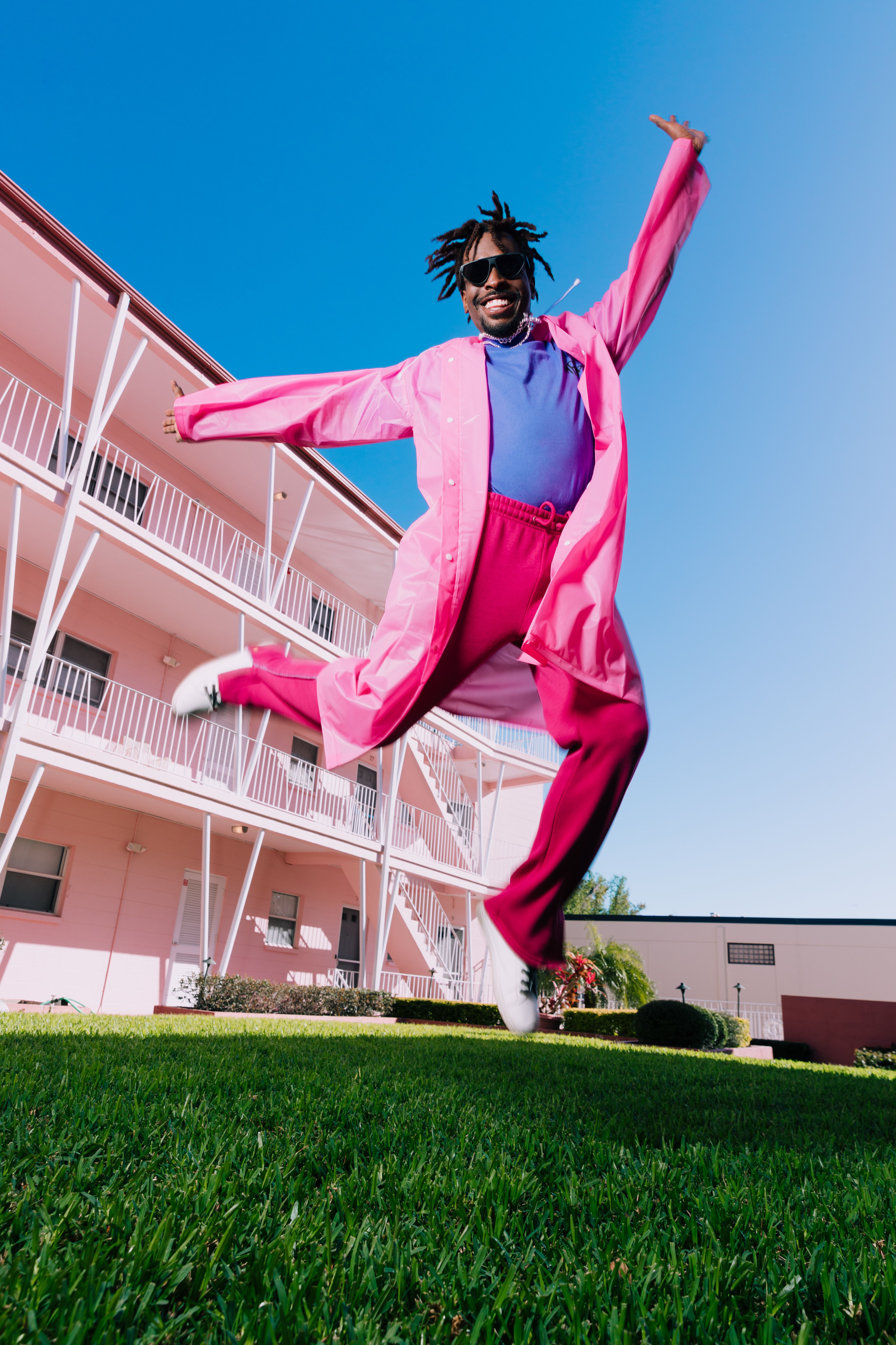 Man in pink outfit joyfully jumps in front of a pink building in Orlando.