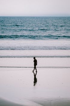 A tranquil scene of a woman walking along Kuta Beach in Bali as the sun sets, creating a beautiful silhouette against the ocean waves.