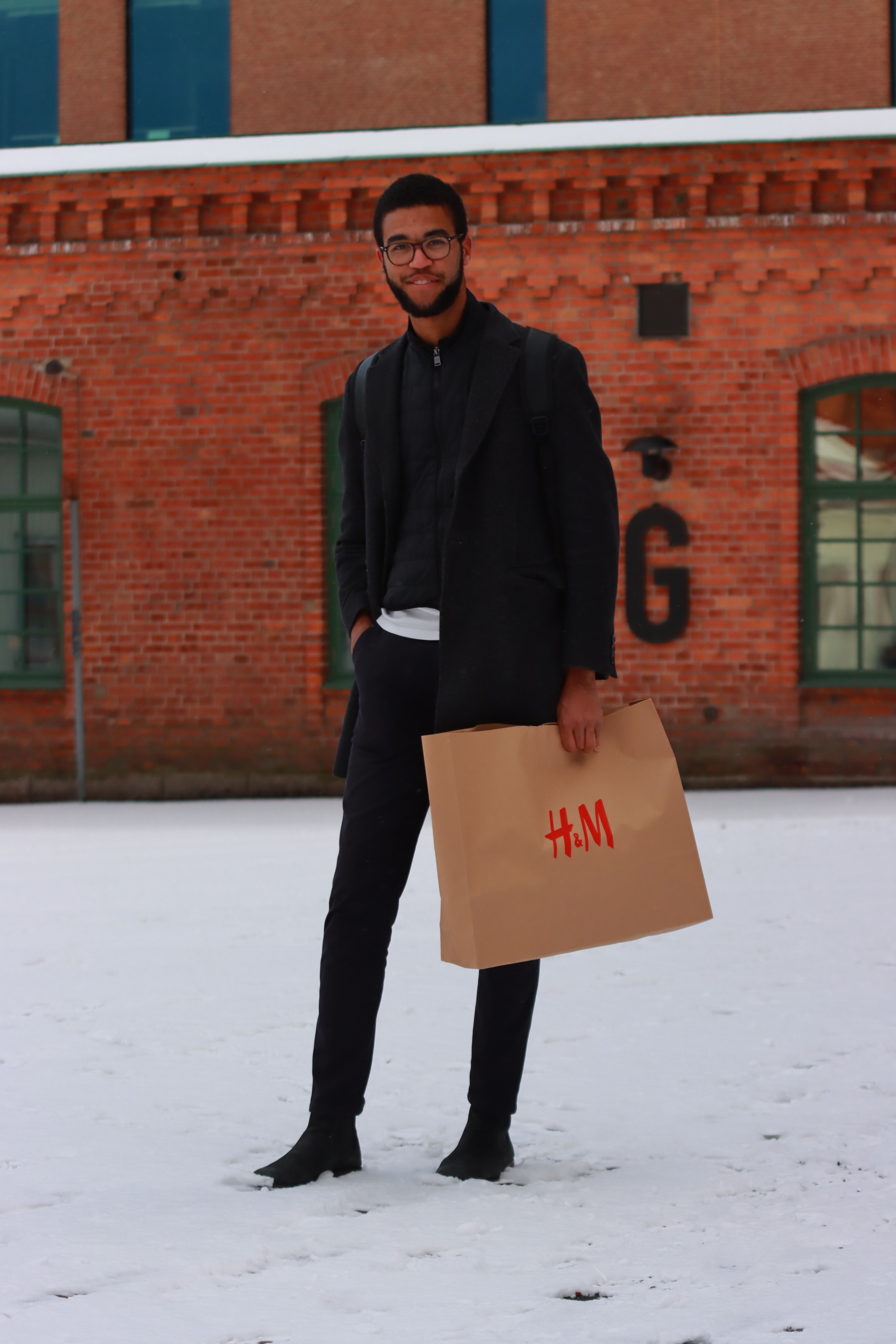Stylish man holding a shopping bag in snowy Jönköping, Sweden.