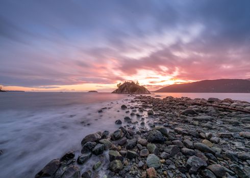 Captivating long exposure shot of a rocky seashore at sunset with vibrant skies.