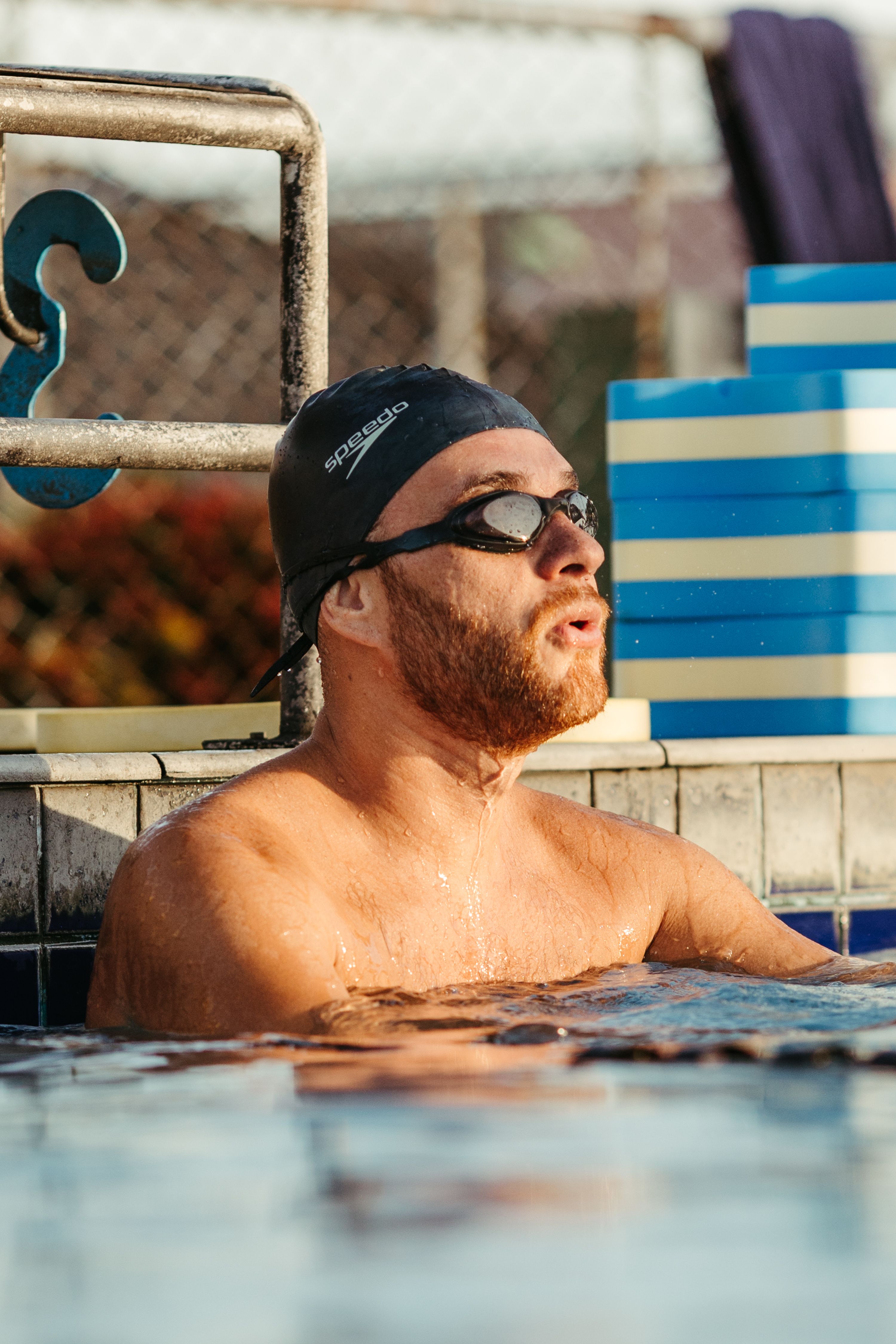 A male swimmer wearing goggles and cap takes a break at the poolside, exhibiting athletic concentration.