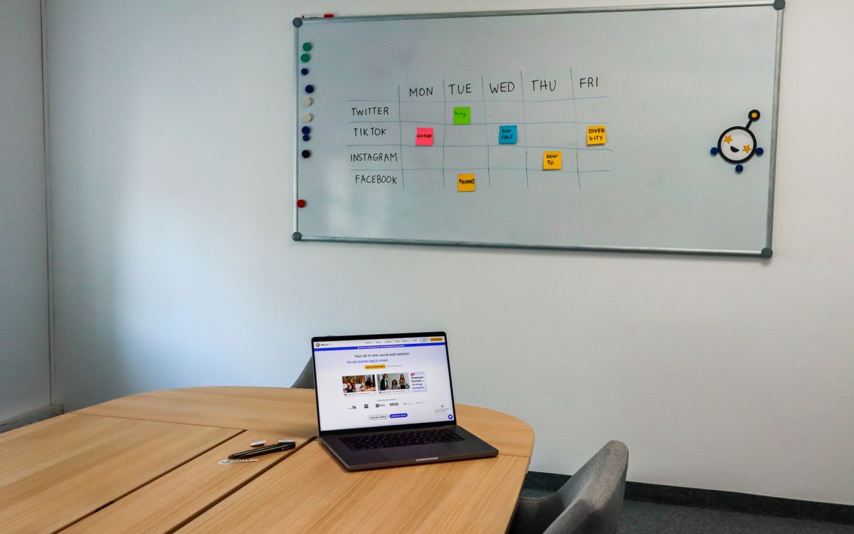 Office setup featuring a conference table, laptop, and organized whiteboard schedule, highlighting a tech-driven workspace.
