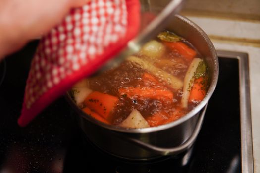 A person cooking vegetable soup with fresh carrots and herbs indoors.