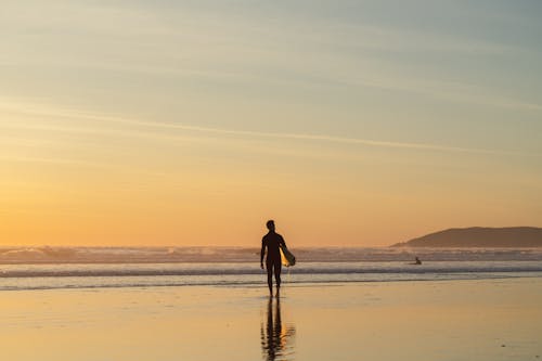 Silhouette of Man with Surfboard on Beach at Sunrise