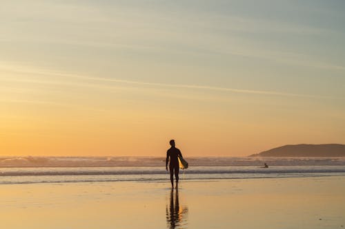 Free Silhouette of Man with Surfboard on Beach at Sunrise Stock Photo