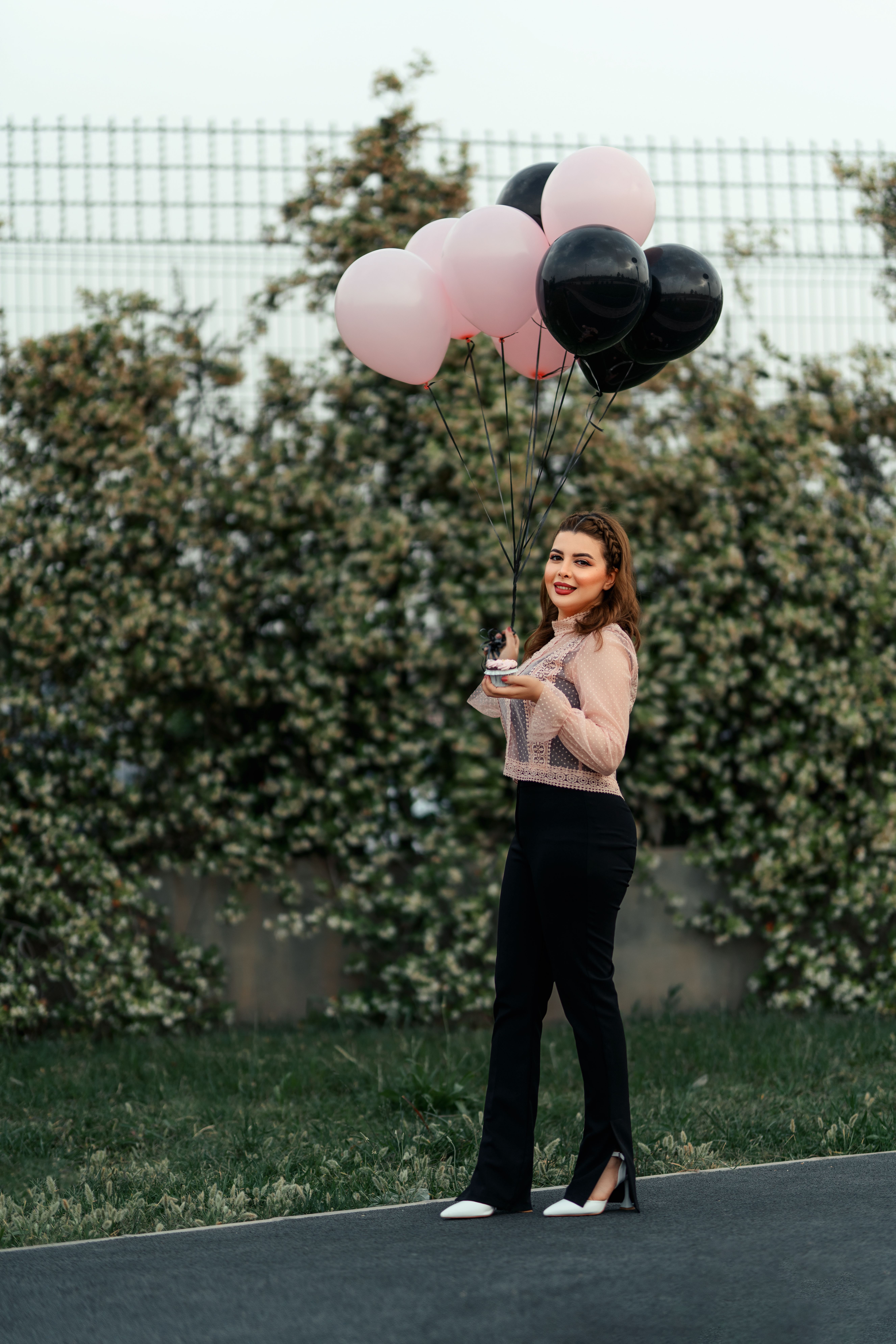 Stylish woman posing with pink and black balloons, creating a fashionable outdoor scene.