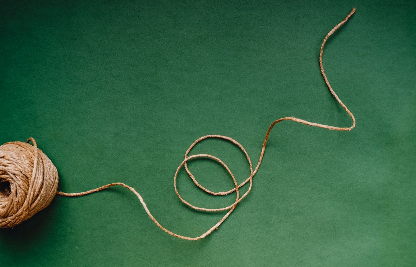 A ball of twine with a loose end on a green background, ideal for craft themes.