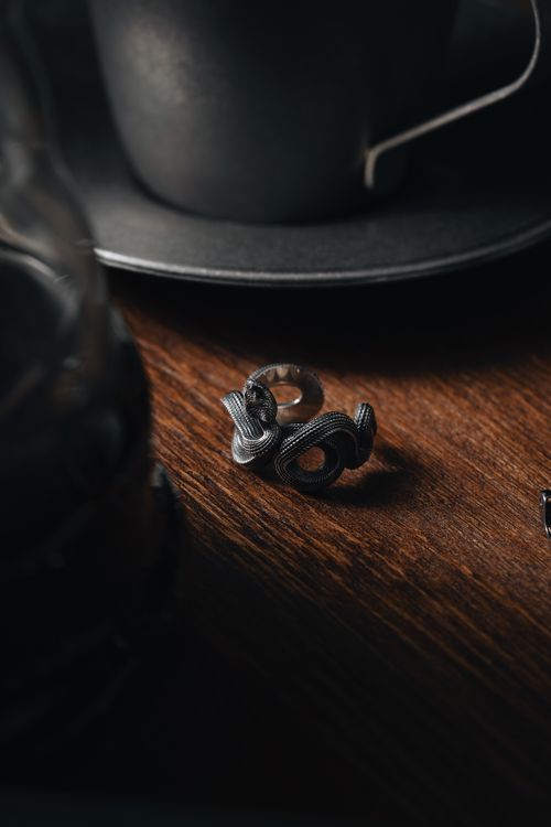 Free Artistic shot of a snake-shaped ring on a wooden table, with a teacup in the background. Stock Photo