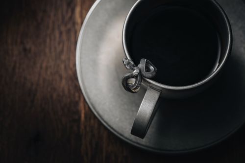 Free A close-up of a teacup with an intricate snake handle on a saucer, showcasing artistic elegance. Stock Photo