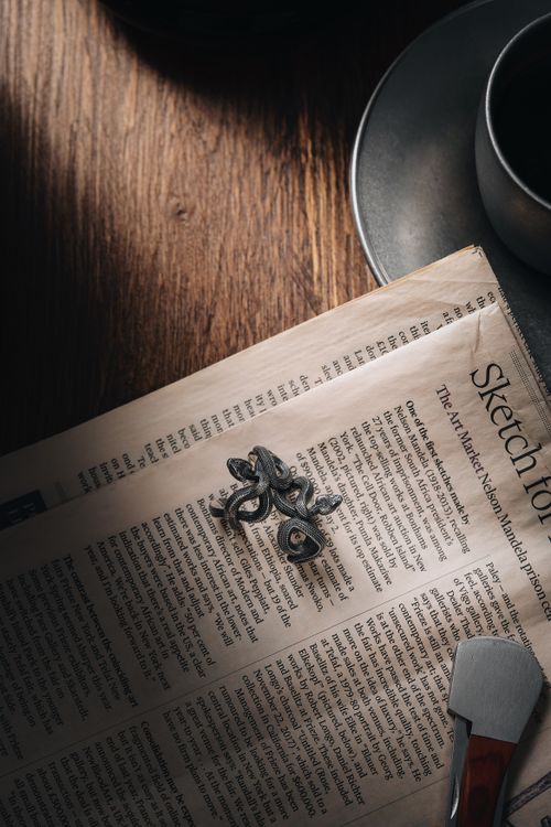 Free A snake shaped ring illuminates a newspaper atop a wooden table, accompanied by a ceramic cup. Stock Photo