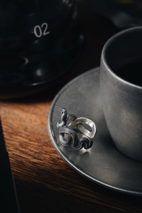 Free Artistic capture of a silver snake-shaped ring on a saucer with a teacup. Stock Photo