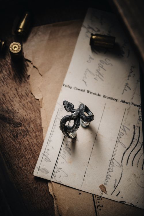 Free Artistic still life of a snake-shaped silver ring on vintage postcard with cartridges. Stock Photo