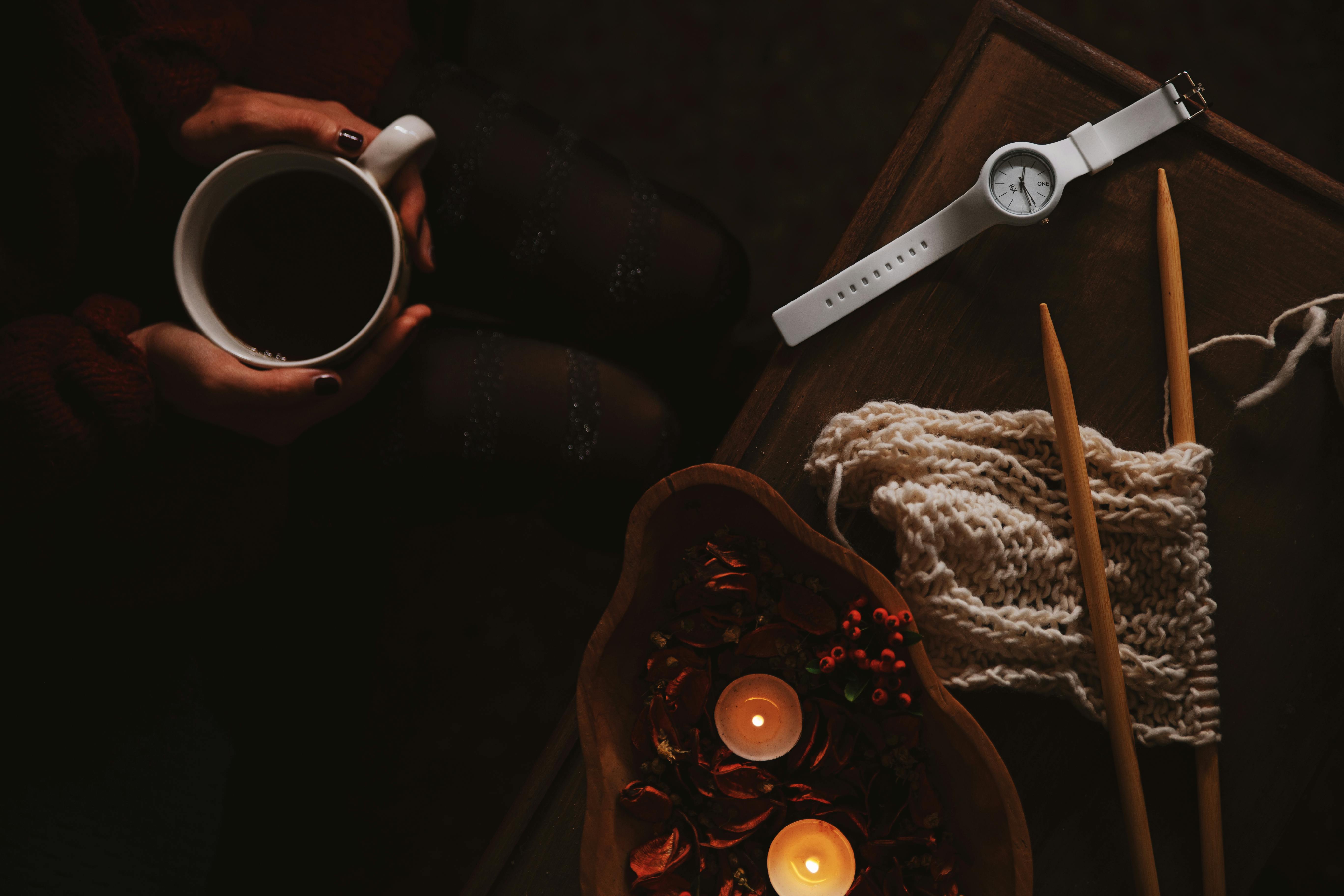 温暖的平地上，咖啡、手表、编织针和蜡烛构成了一幅场景，非常适合室内舒适的时刻