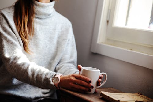 Woman Holding Coffee Mug While Sitting Beside Window