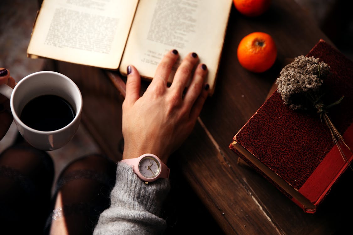 Person Holding Cup of Coffee and Open Book