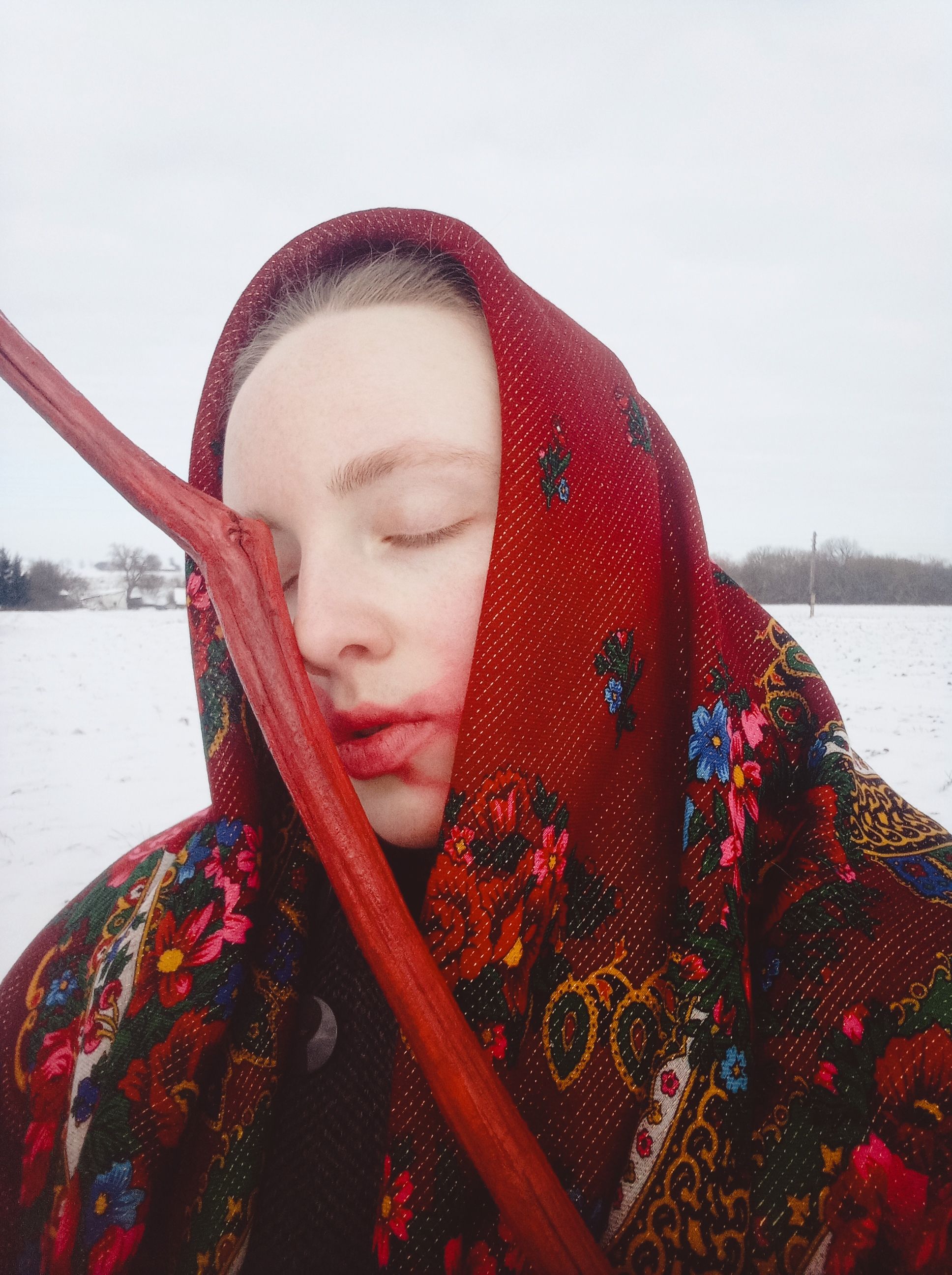 A serene portrait of a woman with closed eyes, wearing a colorful floral headscarf in a snowy landscape.