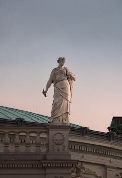 Elegant neoclassical statue atop Burgtheater in Vienna, captured at sunset.