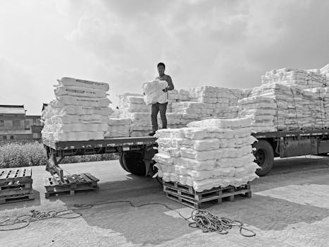 A worker organizes cargo stacks on a truck in an industrial area.