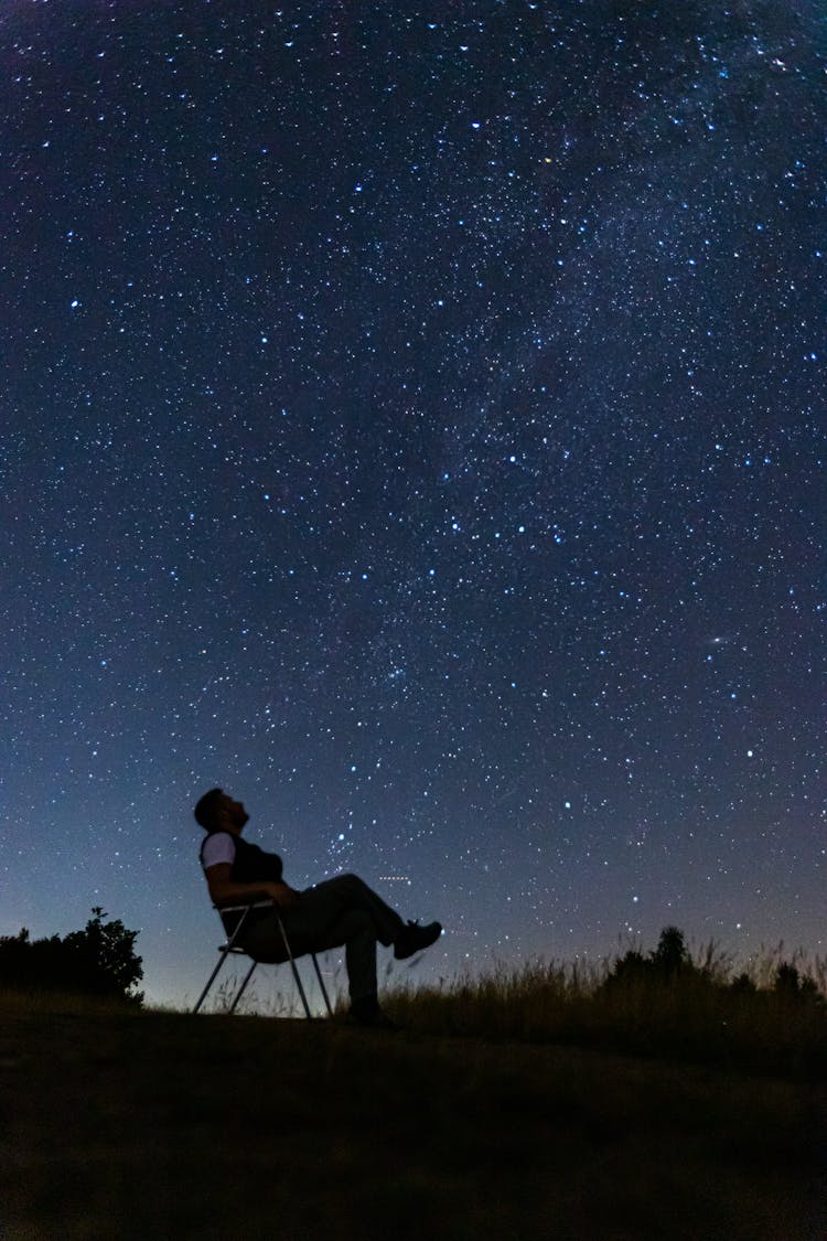 Silhouette Of A Man Sitting On A Hill Under A Starry Night Sky 