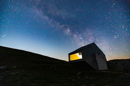 Free A stunning night sky over a lit cabin in Bosna's mountains. Stock Photo
