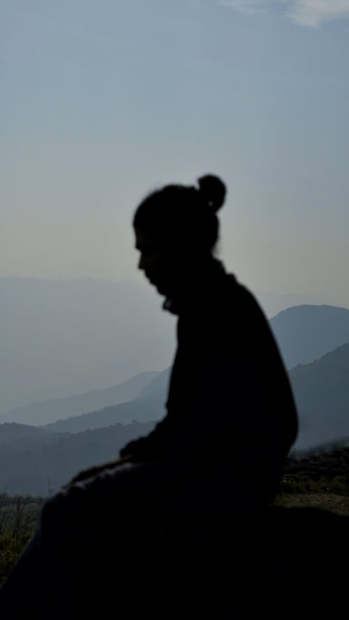 Silhouette of a Person Sitting on a Mountain Peak 