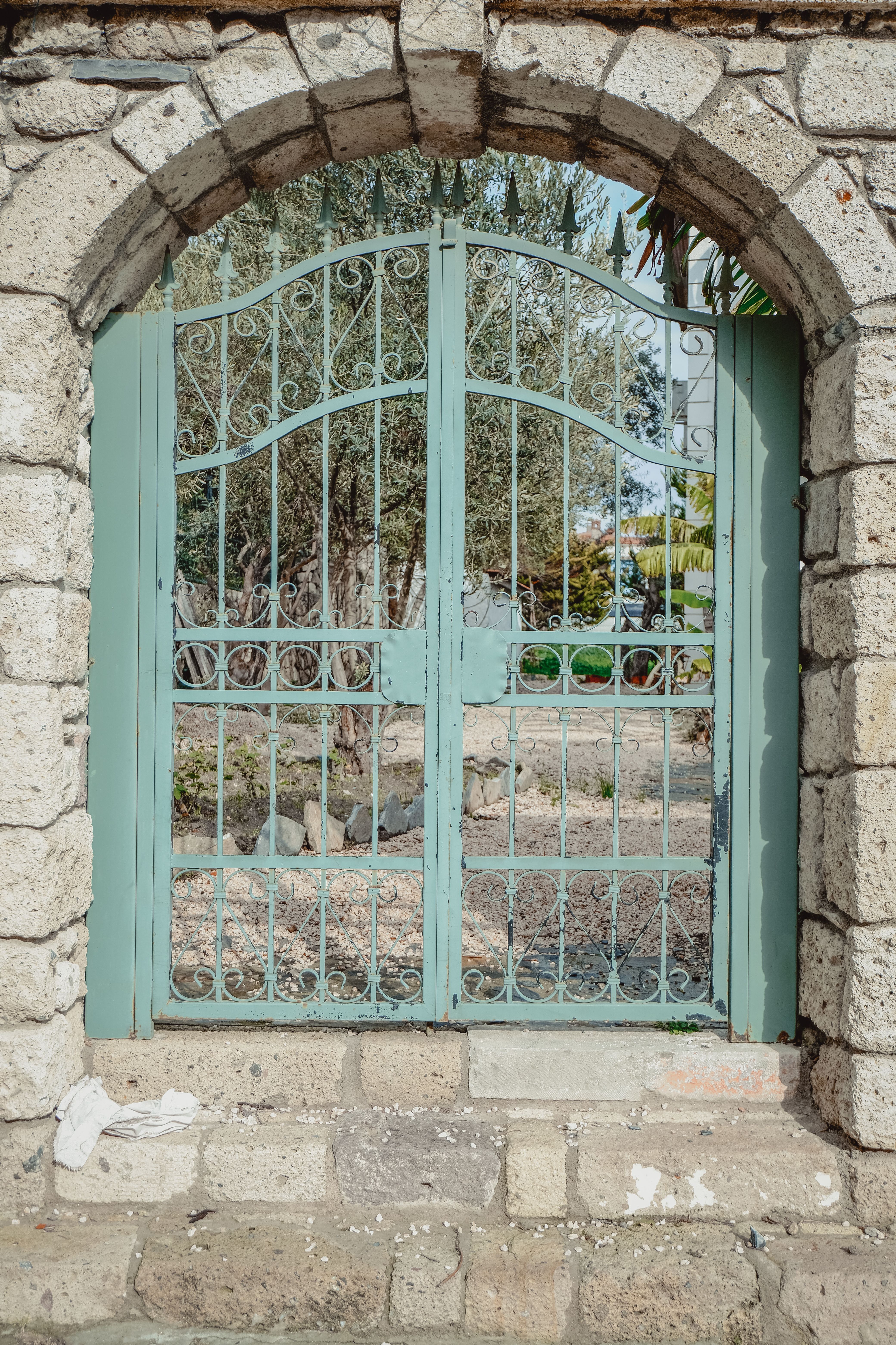 Poartă veche din fier montată într-un arc de piatră rustic, înconjurată de vegetație